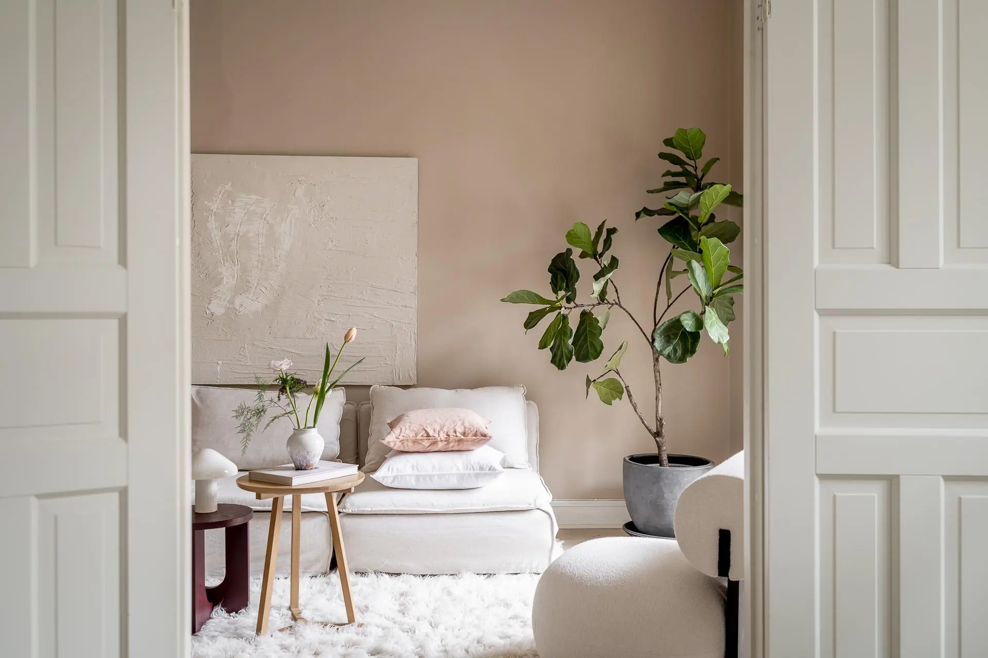 De mooie grote Vioolbladplant voegt een vleugje kleur aan deze stijlvolle beige woonkamer.