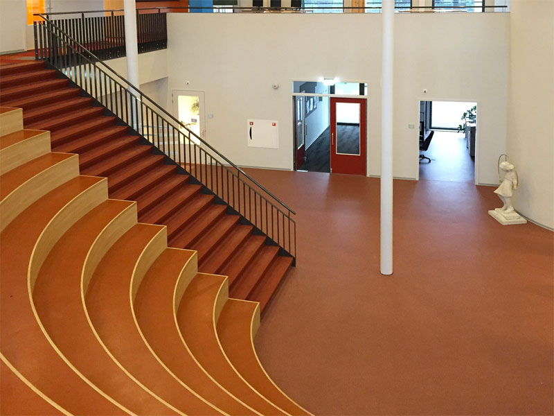 Een grote collegezaal met een rode Unica troffelvloer - Bron: Unicavloeren.nl