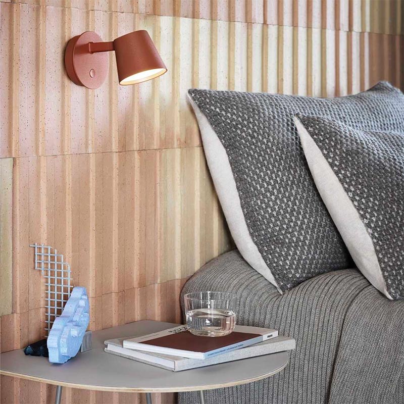 De koperbruine Muuto Tip wandlamp staat prachtig bij de houten wandpanelen in deze moderne slaapkamer.