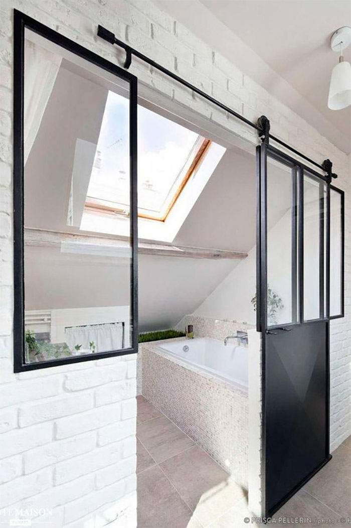 Voor deze kleine badkamer op zolder is er gekozen voor een industriële stalen schuifdeur met glas.