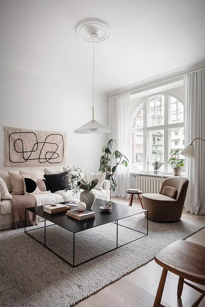 Deze heerlijke woonkamer met witte muren en plafond is verrijkt met mooie aardetinten meubels en accessoires, zoals de taupe fauteuil, kussens en plaid op de witte bank.